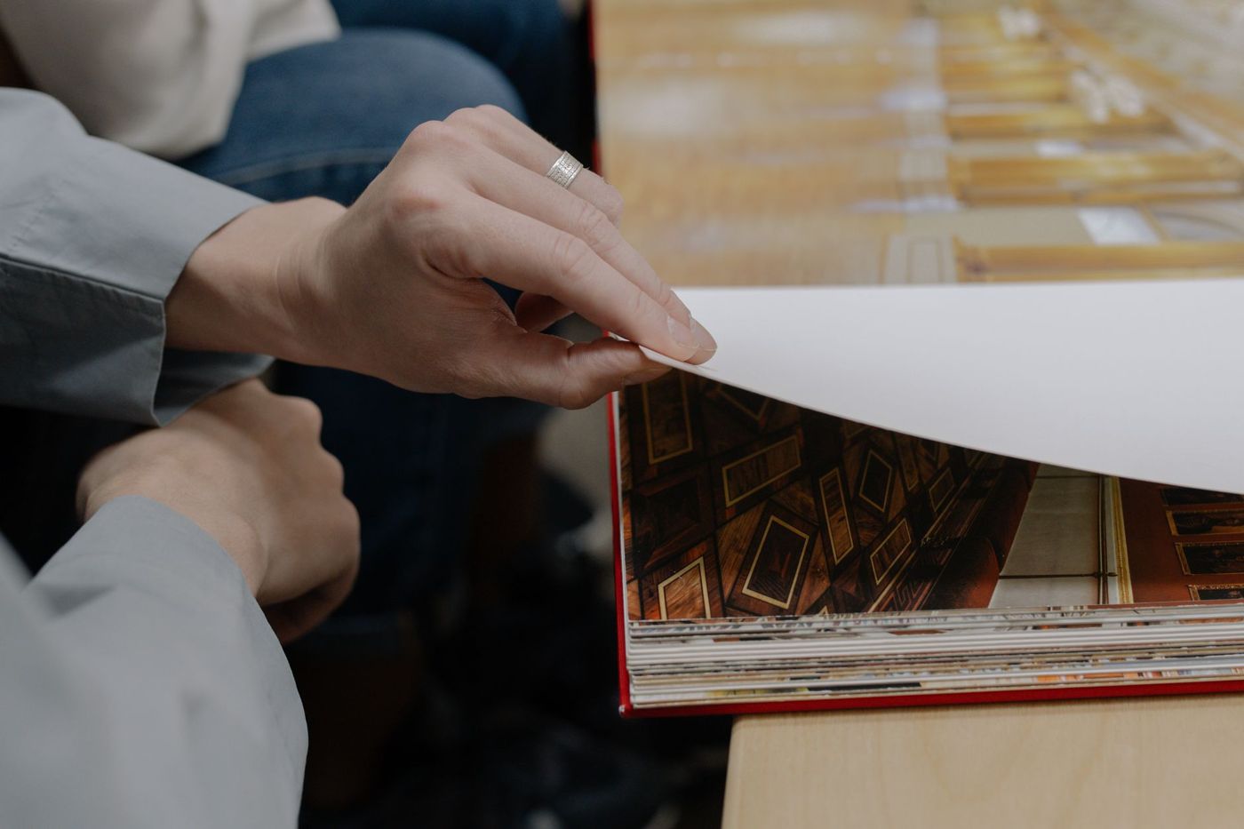 Hands turning a white page in a large photo book bound in red, lying on a wooden table