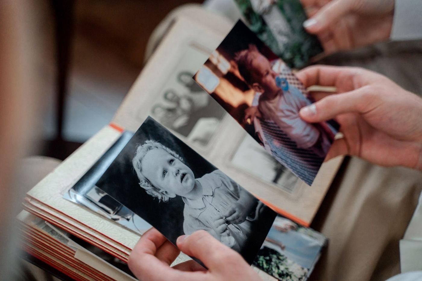 Ruce drží staré černobílé a barevné fotky miminek a batolat nad otevřeným vintage fotoalbem