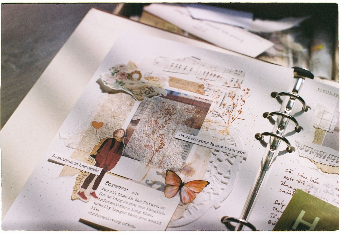 Journal page in a ring binder with a collage of sheet music, flowers, a small figure, a butterfly and word strips