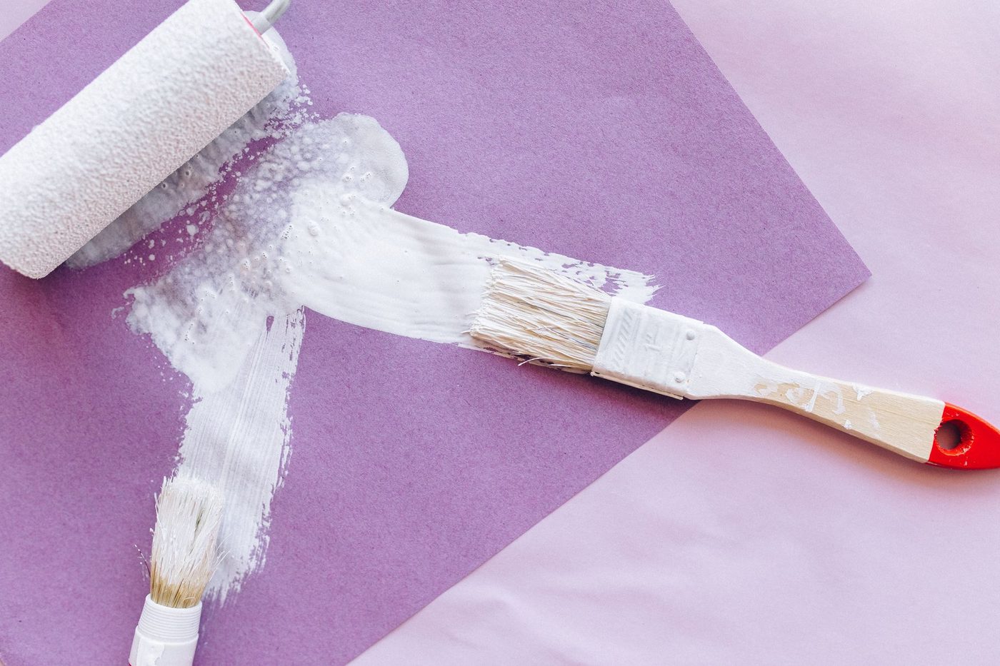 Brush and roller applying a white layer of glue to purple paper