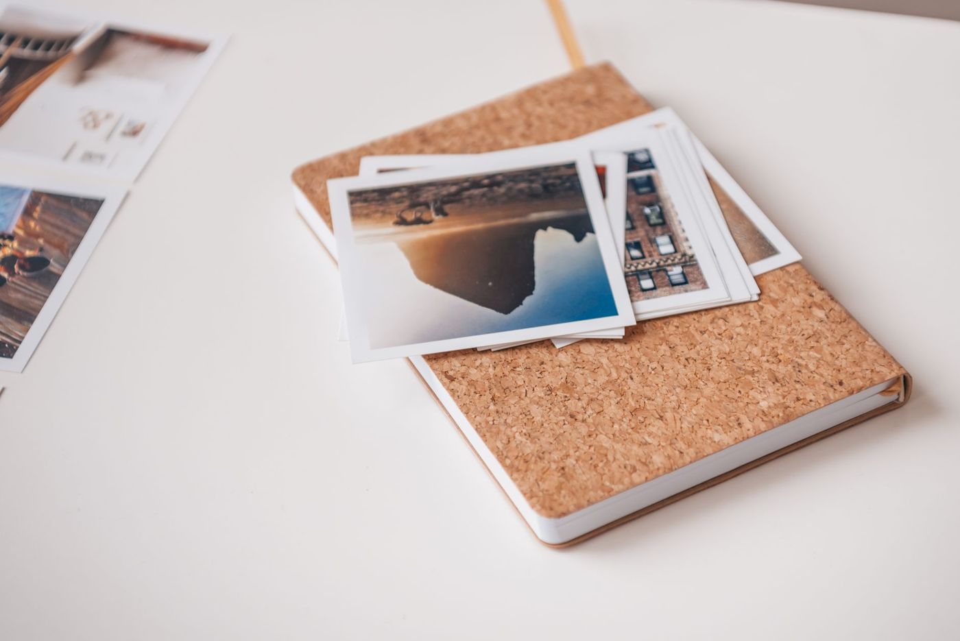 A small stack of white-bordered prints on a notebook with a cork cover, on a white desk