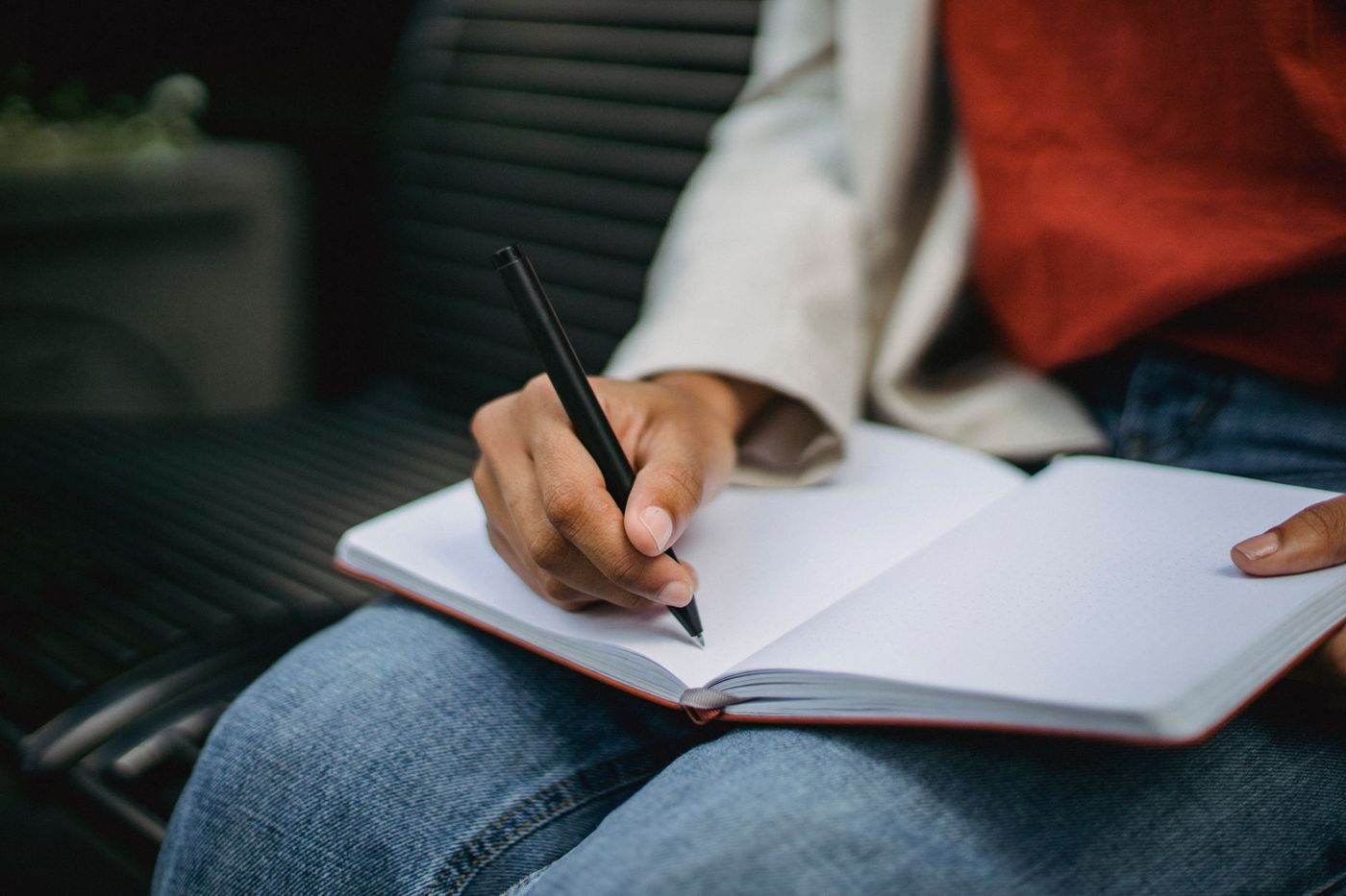 A hand writing with a black pen in an open notebook resting on someone's lap