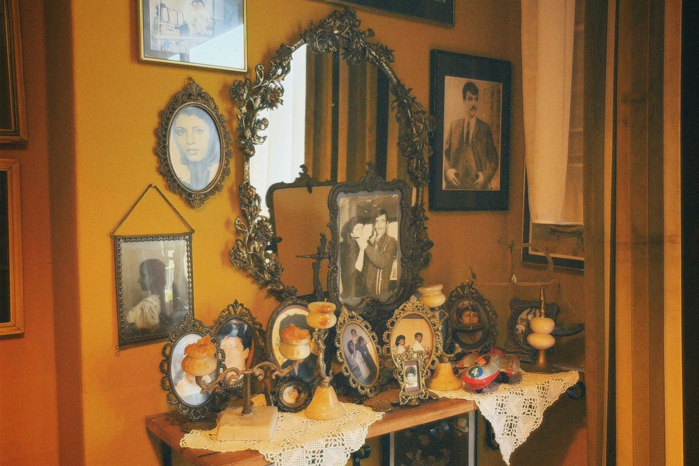 Stol i zid puni starih obiteljskih portreta u ukrašenim okvirima, s crno-bijelim fotografijama muškaraca i žena i čipkom ispod