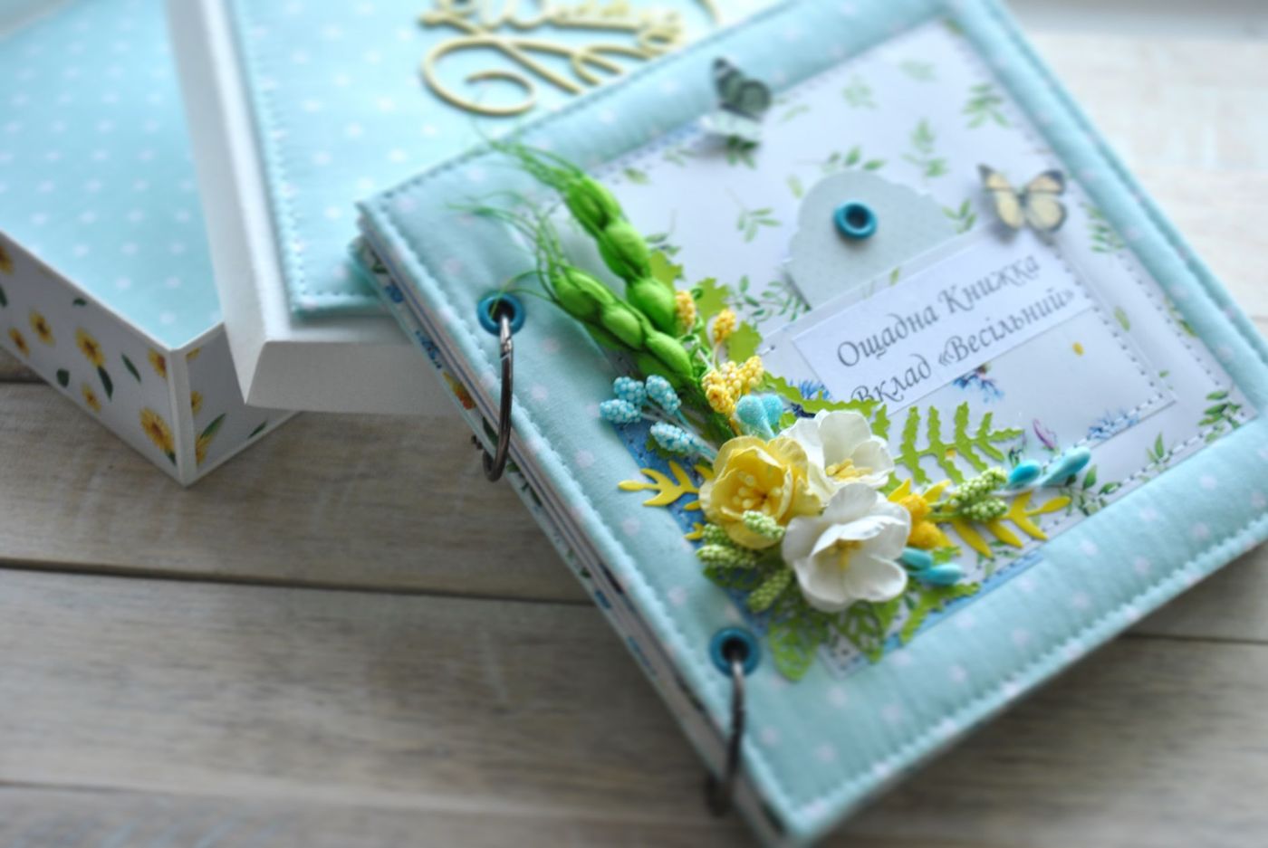 Handmade album in light blue fabric with white polka dots, rings and a bouquet of paper flowers and butterflies on the cover