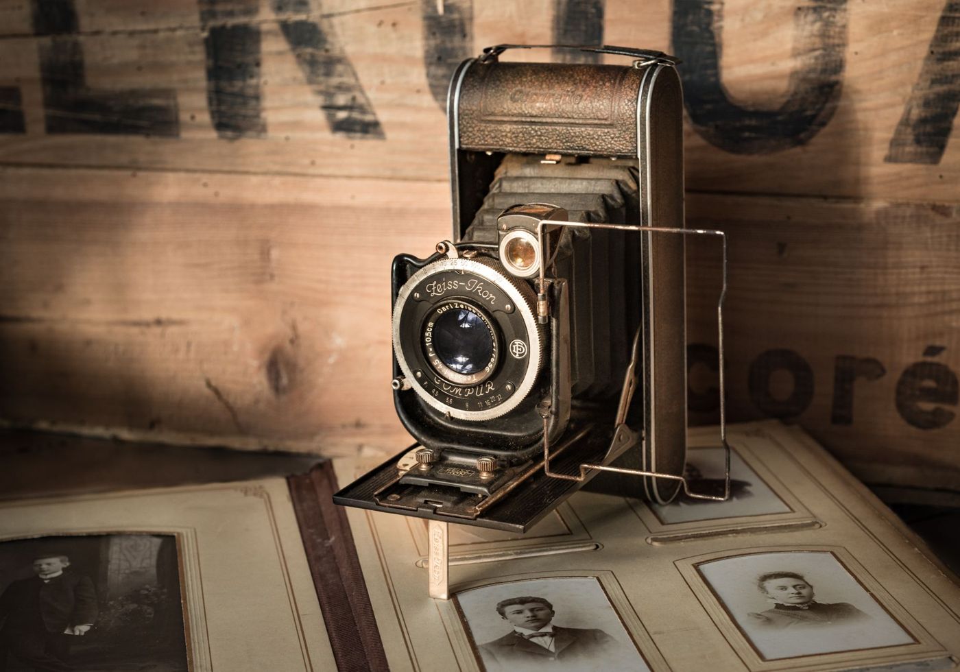Stari sklopivi fotoaparat Zeiss Ikon na otvorenom albumu sa sepija portretima na kartonu, uz drveni sanduk