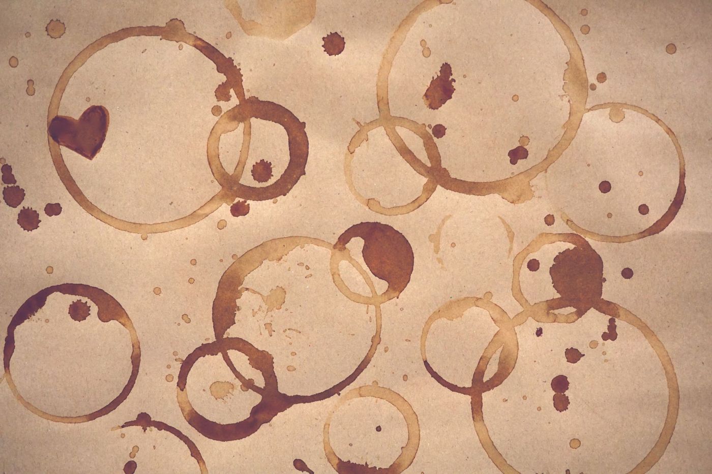 Brown coffee rings and splashes of different sizes on kraft paper, with a heart-shaped stain in the top left