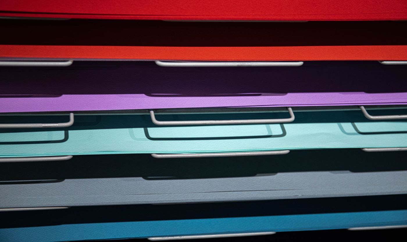 Close-up of stacks of coloured paper in red, purple, turquoise and blue on metal racks
