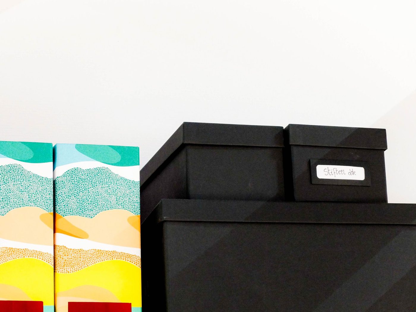 Stacked storage boxes with a label, next to colourful boxes