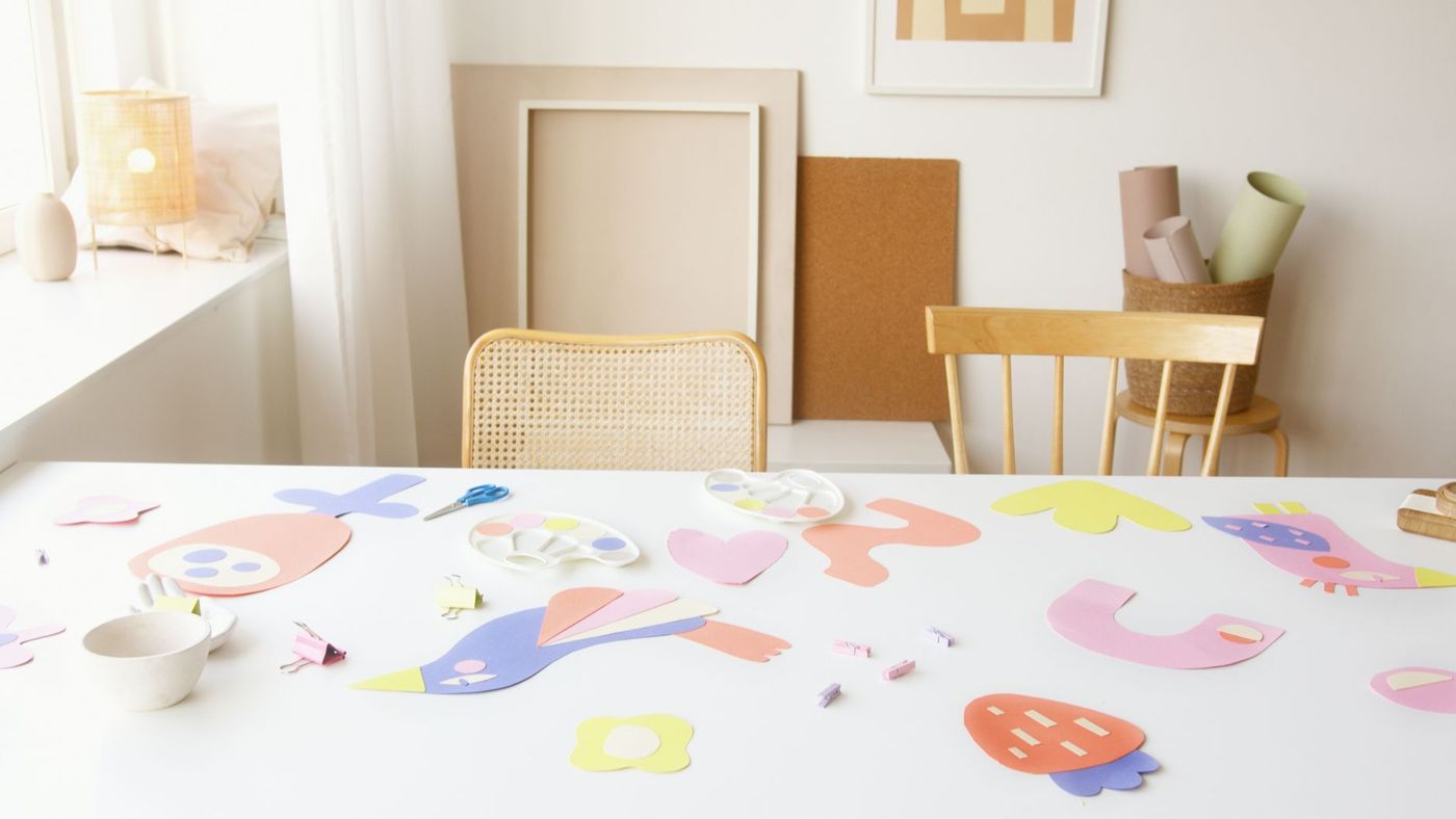 White table with pastel cut-out paper shapes, a pair of scissors and small pegs by a window