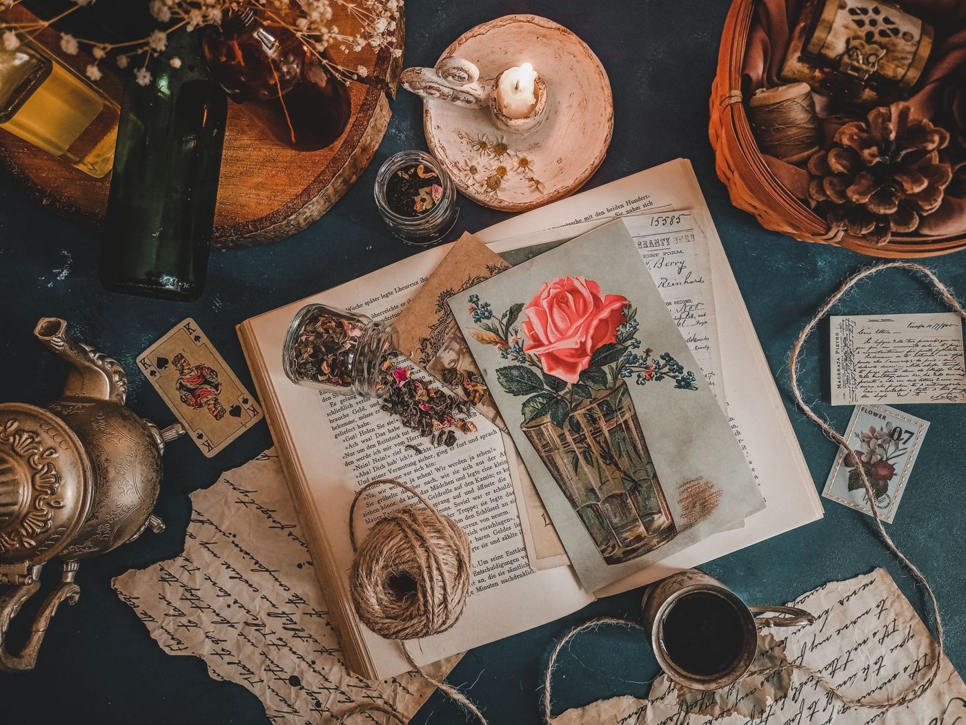 Overhead view of an old book with a rose postcard, handwritten notes, string, a candle and a teacup
