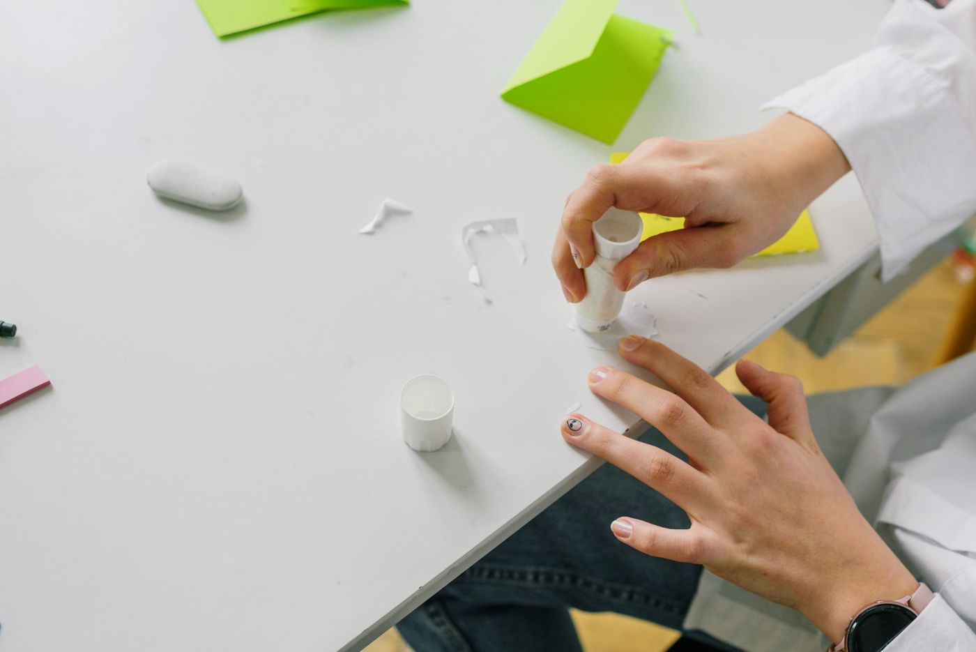 Due mani tengono una colla stick sopra un pezzo di carta su un tavolo bianco, con biglietti verdi e una gomma