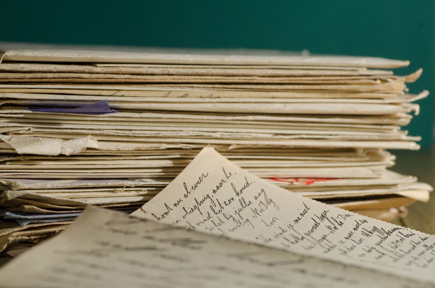 Pile of old, yellowed letters and envelopes, with a handwritten sheet in the foreground against a green background